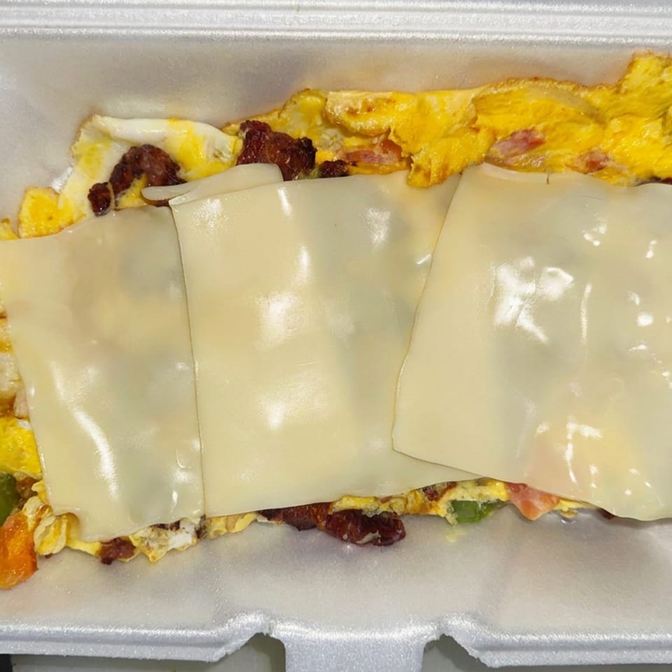 Cheesy breakfast omelet with bacon, sausage, and vegetables in a white foam takeout container.